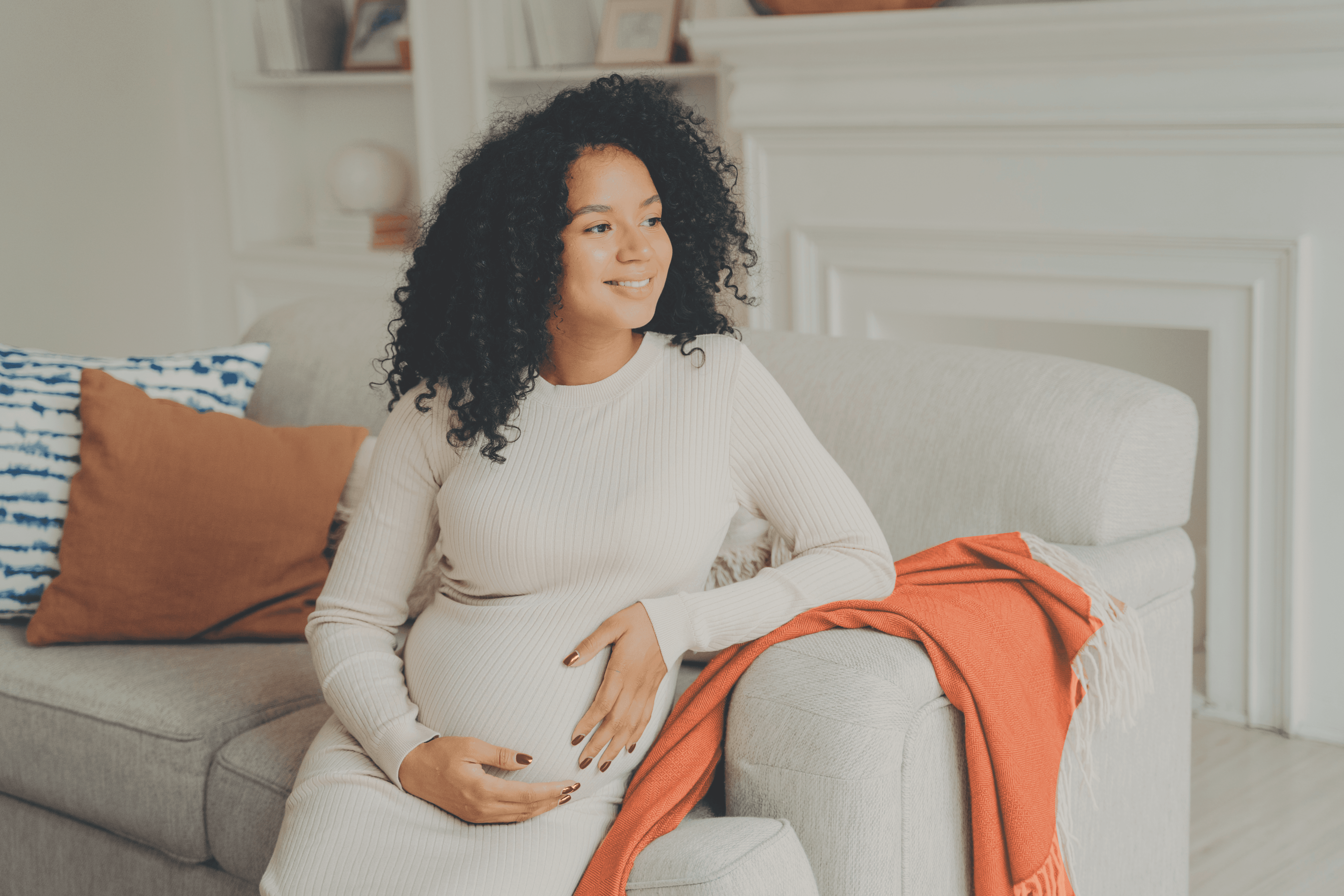 Pregnant woman sitting on a couch at home with her hands resting on her baby bump